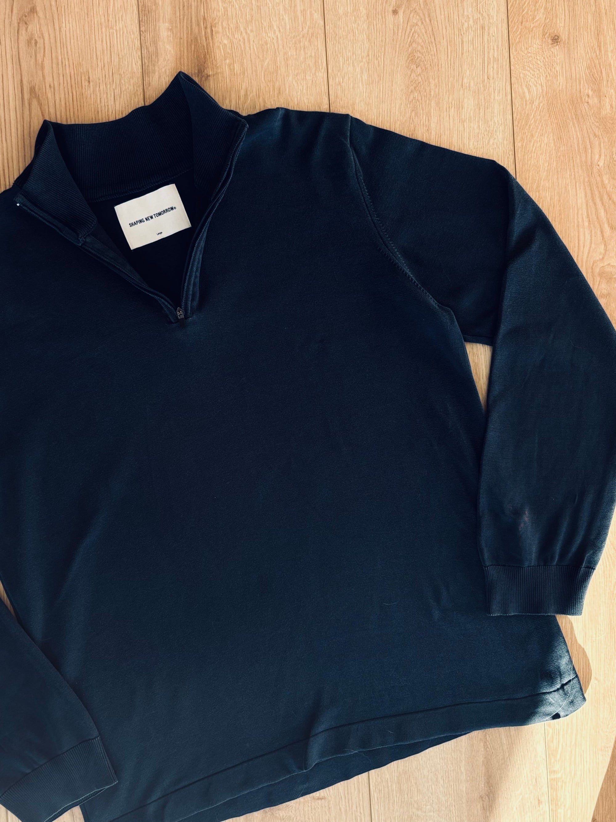 Sort sweatshirt fra Fabricobe med quarter zip og stretchmateriale, vist på model foran neutral baggrund.